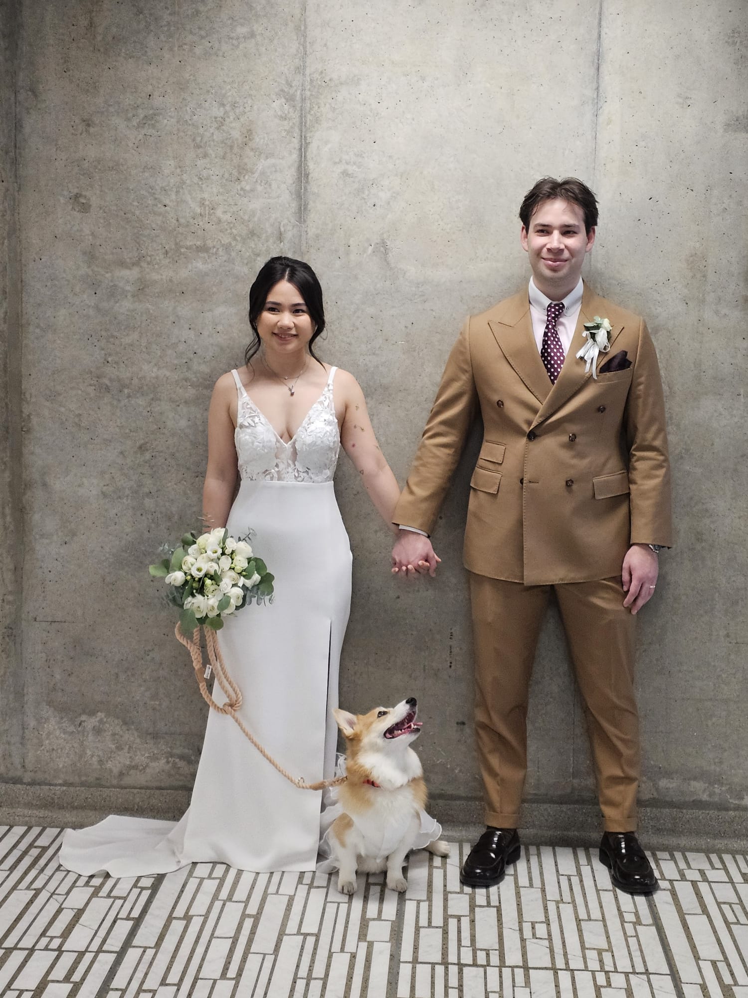 Bride and groom in a tan suit standing together with their dog